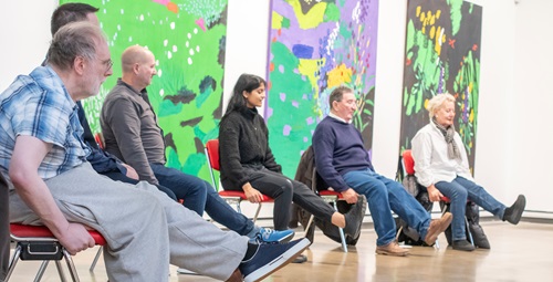 Members of the public seated in an art gallery, doing mobility exercises.
