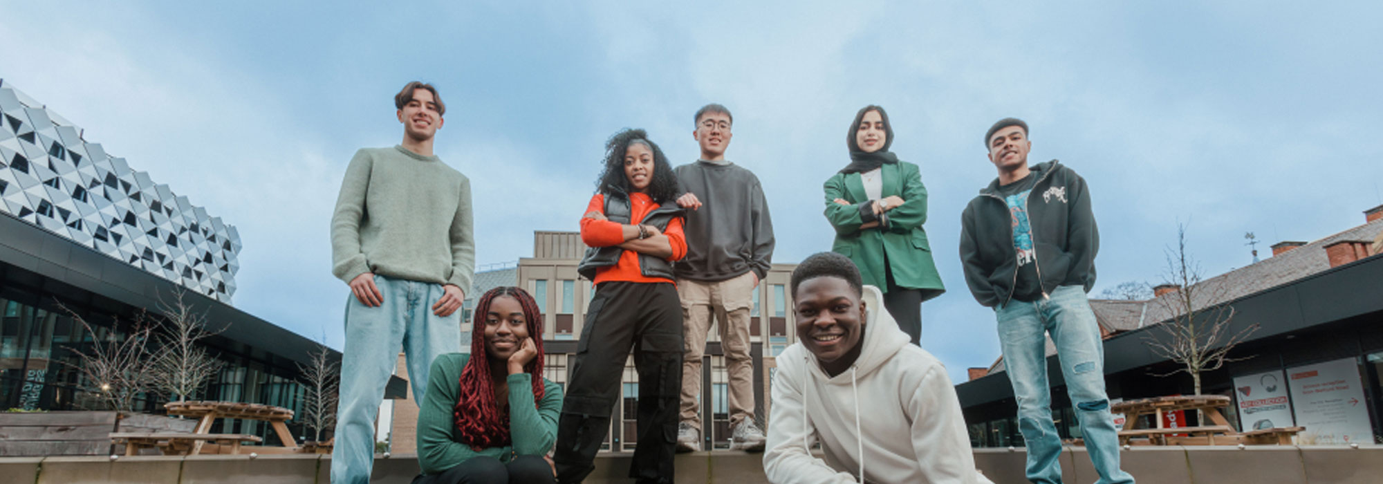 Students smiling with a backdrop of the University of Leicester campus.