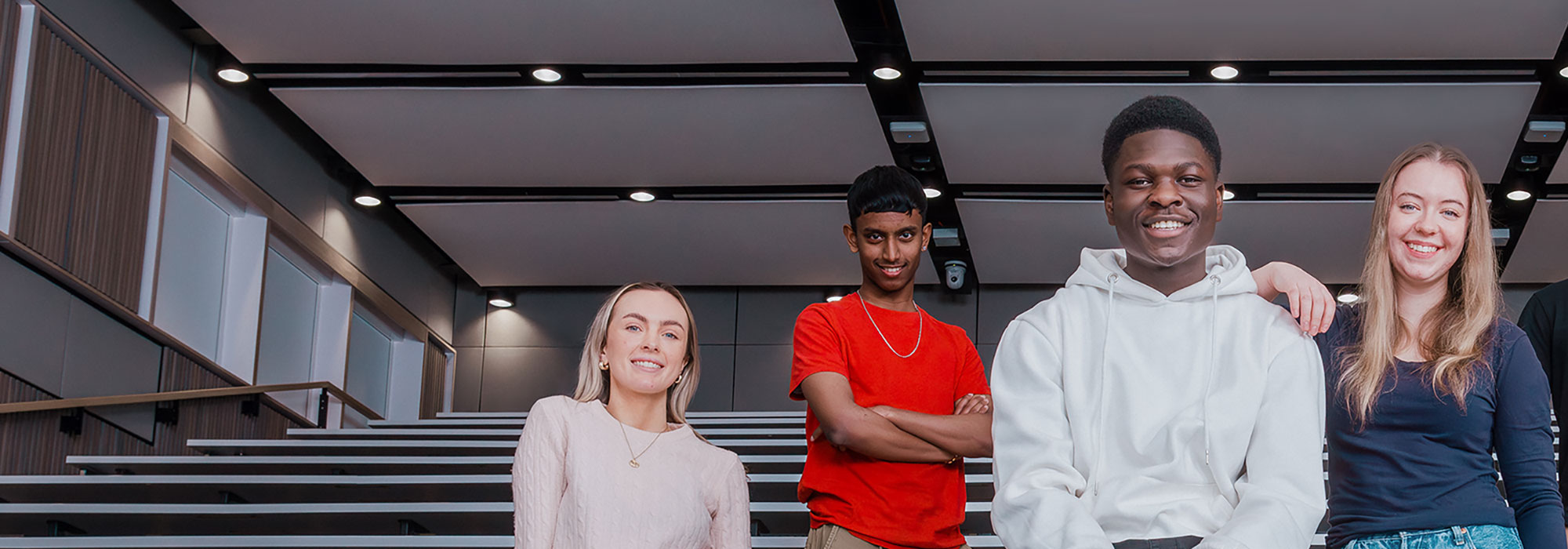 Two male and two female students in a lecture theatre smiling and looking towards the camera