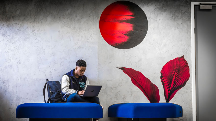 Student sitting in a communal area working on a laptop.