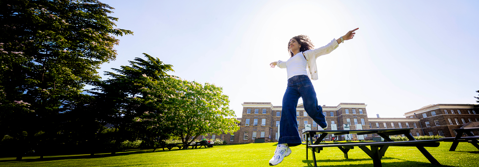 Leicester campus green lawn, on a bright sunny day, smiling student stepping off bench