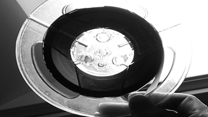 Close-up of a person grasping an acetate reel, typically used in audio production.