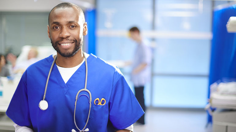 a mid adult doctor looks to camera on the hospital ward, smiling.