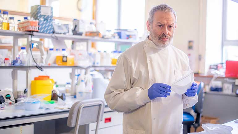 man in white coat in a lab holding a mask