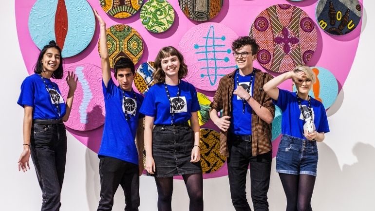 A group of young people smiling in front of a modern art installation.