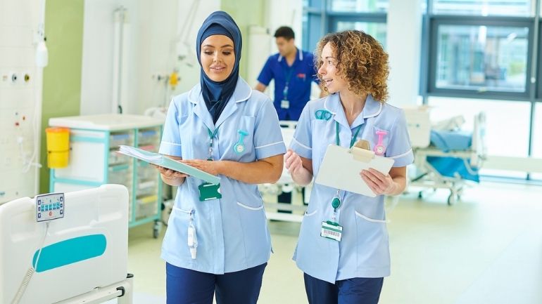 Two healthcare workers share a conversation as they walk through a hospital ward.