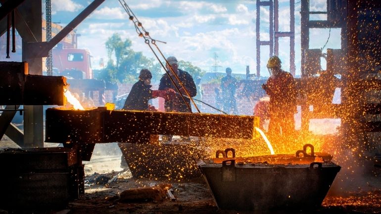 Workers at a steel mill pour molten metal into a container.