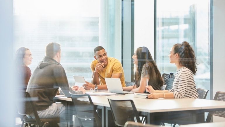 A diverse group of students in conversation around a table.