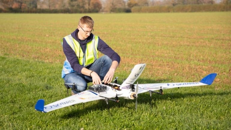 An engineer prepares a drone for take off in an open field.