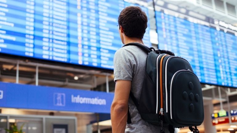 A young man wearing a backpack looks up at an airport departures board.