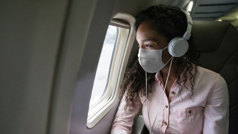 A woman wearing a face mask and headphones onboard an aeroplane.