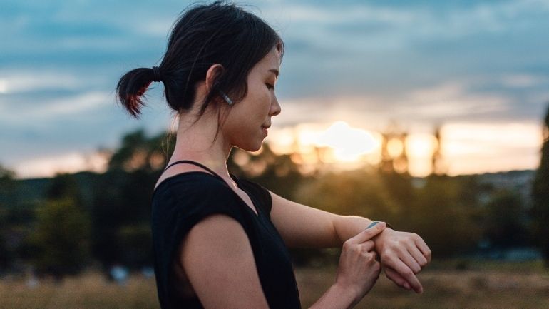 A young woman with earphones checks her smart watch while exercising.