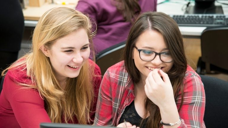 Two smiling students using a computer.