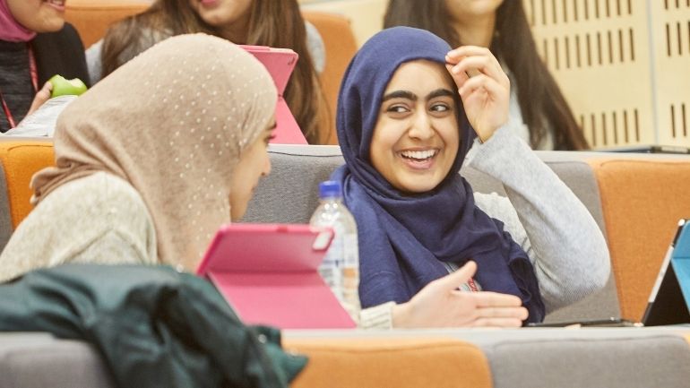 Two female students wearing hijabs share a joke.