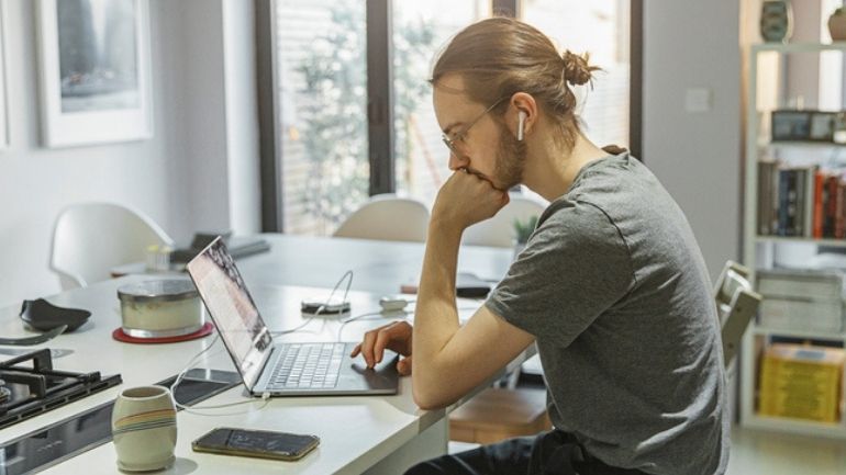A man works from a laptop in a home kitchen.
