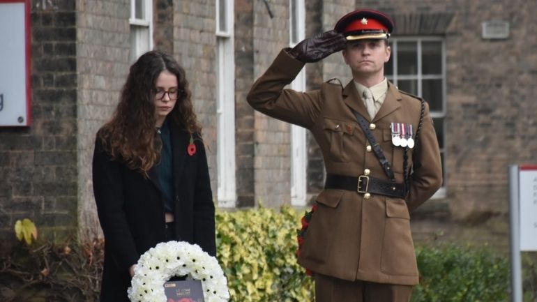 Rhiannon Jenkins, head bowed, with white poppy wreath as Major Ed Matts salutes.