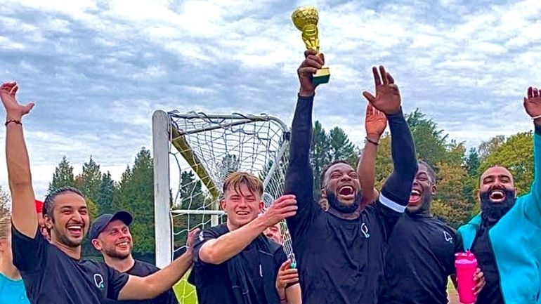 A group of football players celebrate and raise a golden trophy into the air.