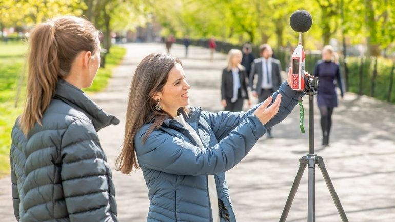 Two scientists hold a microphone in the air to measure noise pollution.