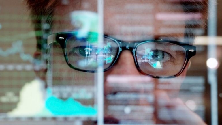 A scientist looks at a series of figures and graphs on a glass screen.