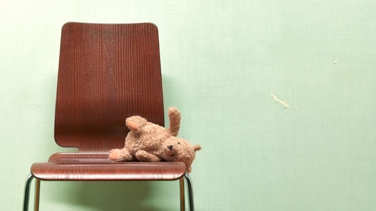 A fallen teddy bear on an empty chair.