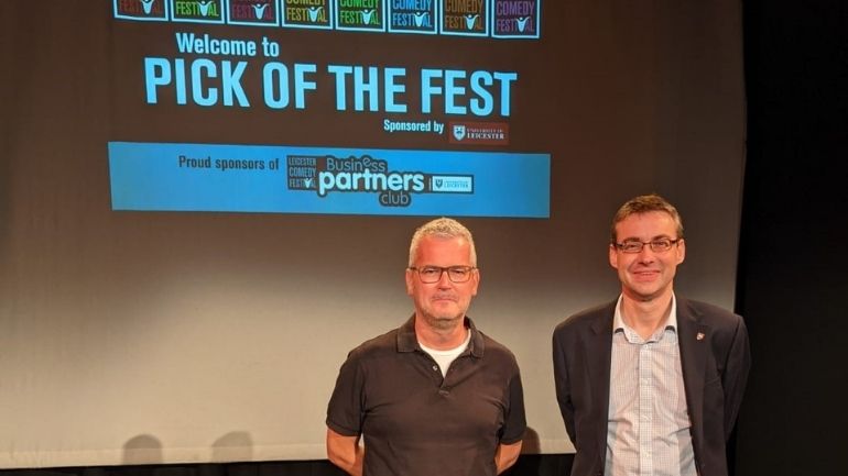 Geoff Rowe and Martyn Riddleston stood in front of branding for Leicester Comedy Festival's Business Partners' Club.