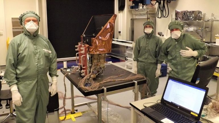 Three individuals in protective clothing pose in front of SMILE's Soft X-ray Imager structural and thermal model.
