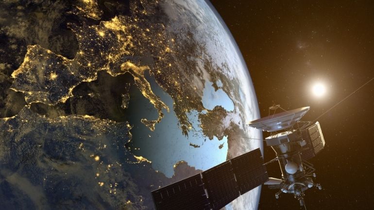 A satellite orbits the Earth, with night-time lights of Europe in the background.