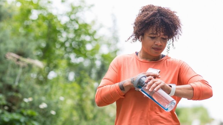 A woman in exercise clothing checks a wearable pedometer on her wrist.