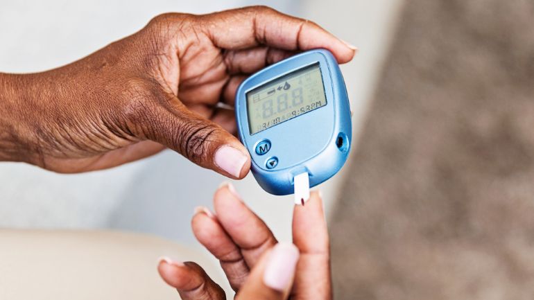 A Black woman uses a blood sugar monitor.