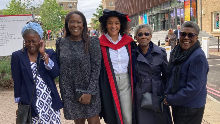 Dr Naomi-Rowe Gurney in graduation robes with family on the University of Leicester campus.