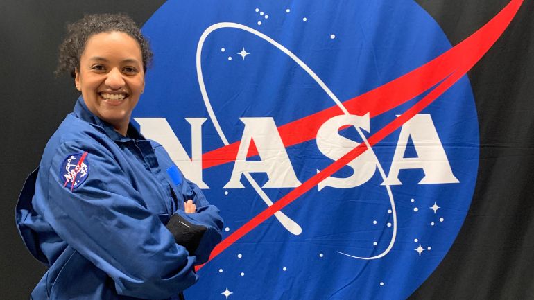 Dr Naomi-Rowe Gurney poses in front of a large NASA logo.