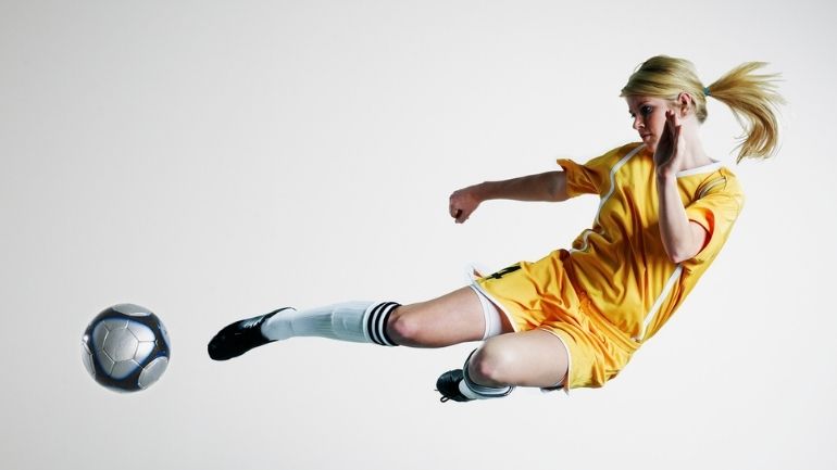 A female footballer in mid-air as she looks to volley the ball.