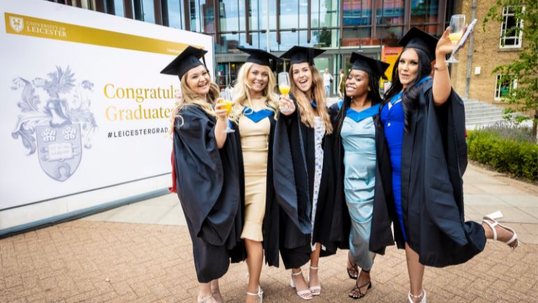Five students celebrate their graduation in front of the Percy Gee Building.