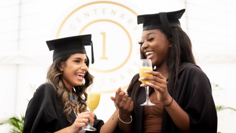 Two students toast their graduation with a drink.