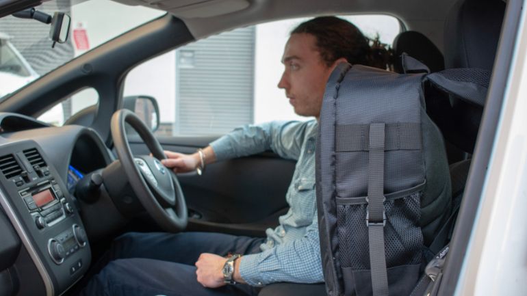 An air quality sensor attached to the passenger seat of a car, with the male driver in the background.