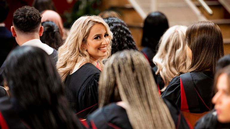 A University of Leicester graduate smiles among a crowd of students.