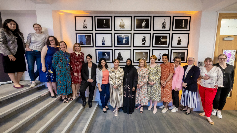 Picture of the inspirational women standing in front of the wall of portraits.