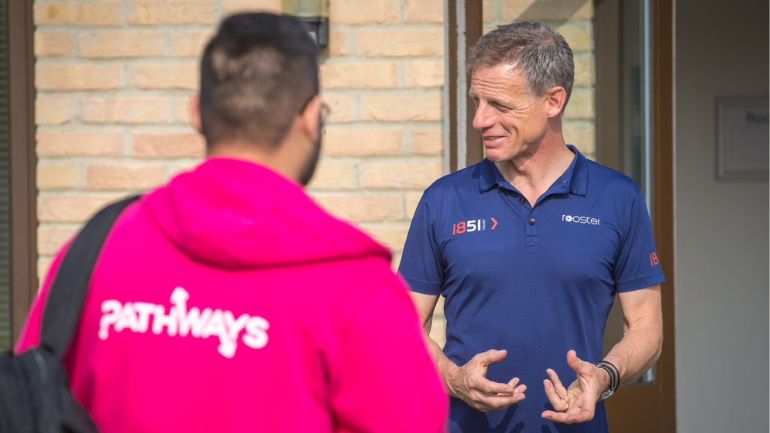 A man talks to an unseen group, with a student ambassador wearing a pink Pathways hoodie in the foreground.