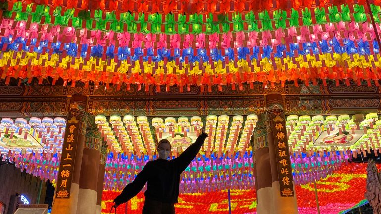 Student in celebratory pose in front of colourful lanterns at a South Korean market.