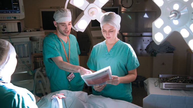 Two Operating Department practitioners discuss a patient's records in an operating theatre setting.