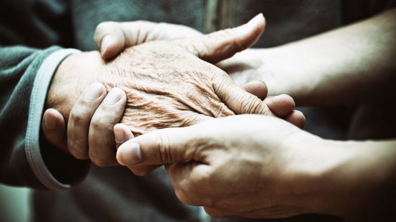 Close up of the hands of a health worker comforting a patient with dementia.