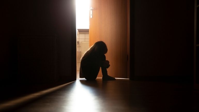 A child sitting on the floor on their own in a dark hallway.