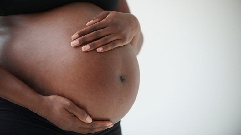 A Black woman holds her bump during pregnancy.