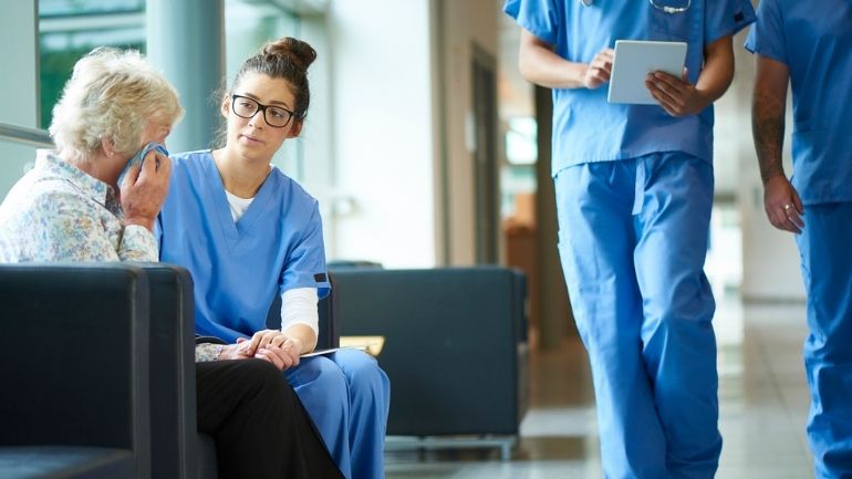 A healthcare worker comforts a patient while sat on a sofa.
