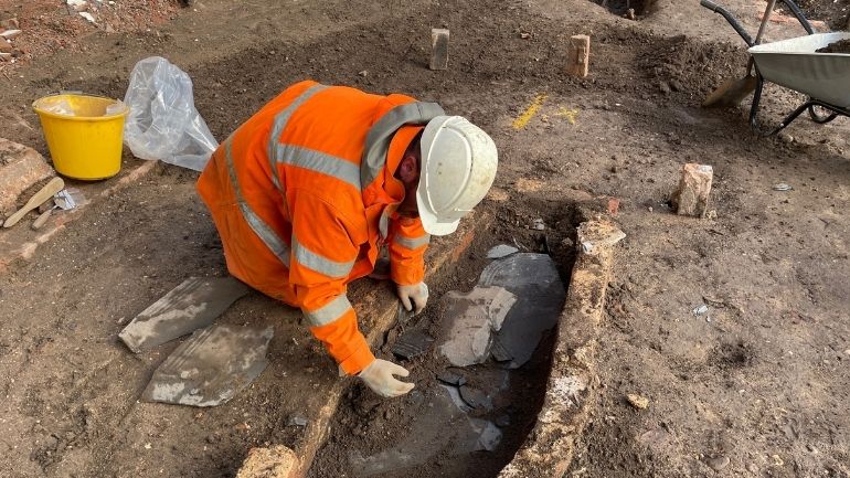 Archaeologist excavates a broken headstone from a brick lined grave at Leicester Cathedral.