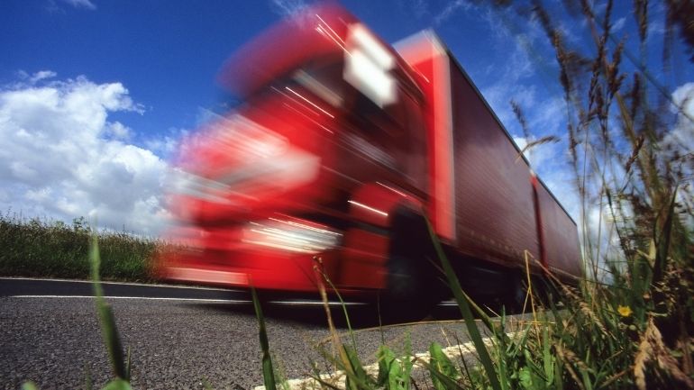 A red lorry drives down a UK country road.