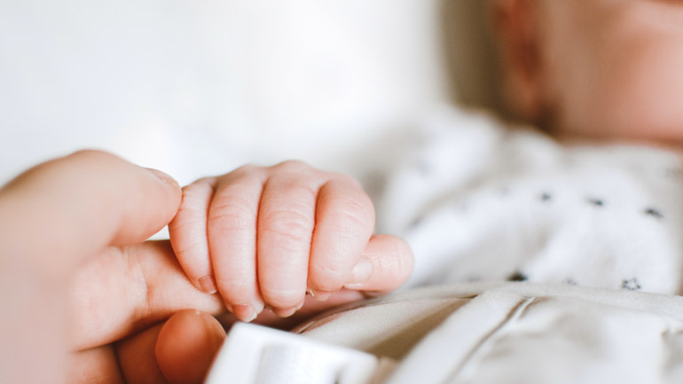 A baby grips a parent's finger.