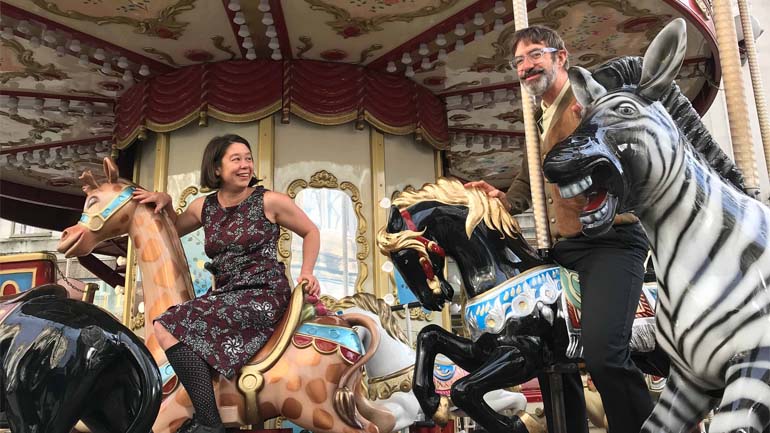Jo Fong and George Orange smile on a merry-go-round