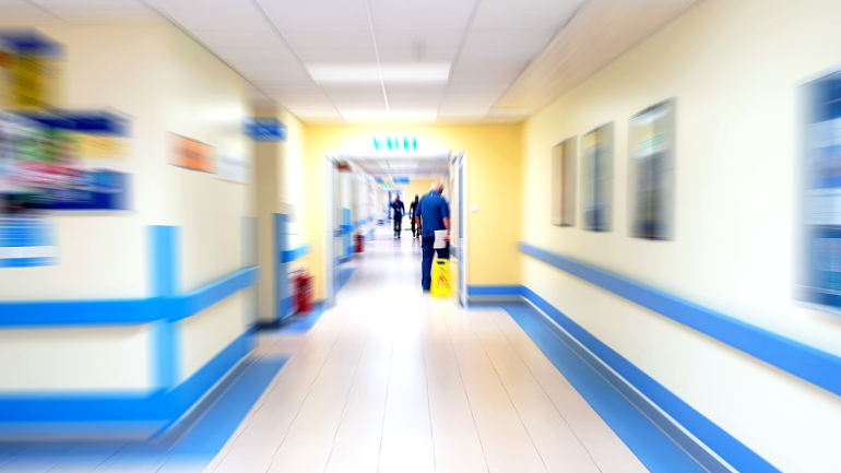 A blurred photo of a hospital corridor leading to a ward.