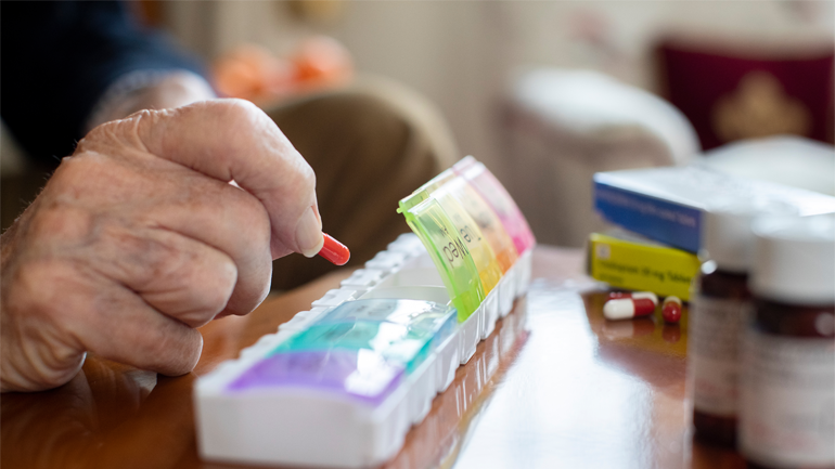 Elderly person placing pills into a colourful pill organiser.